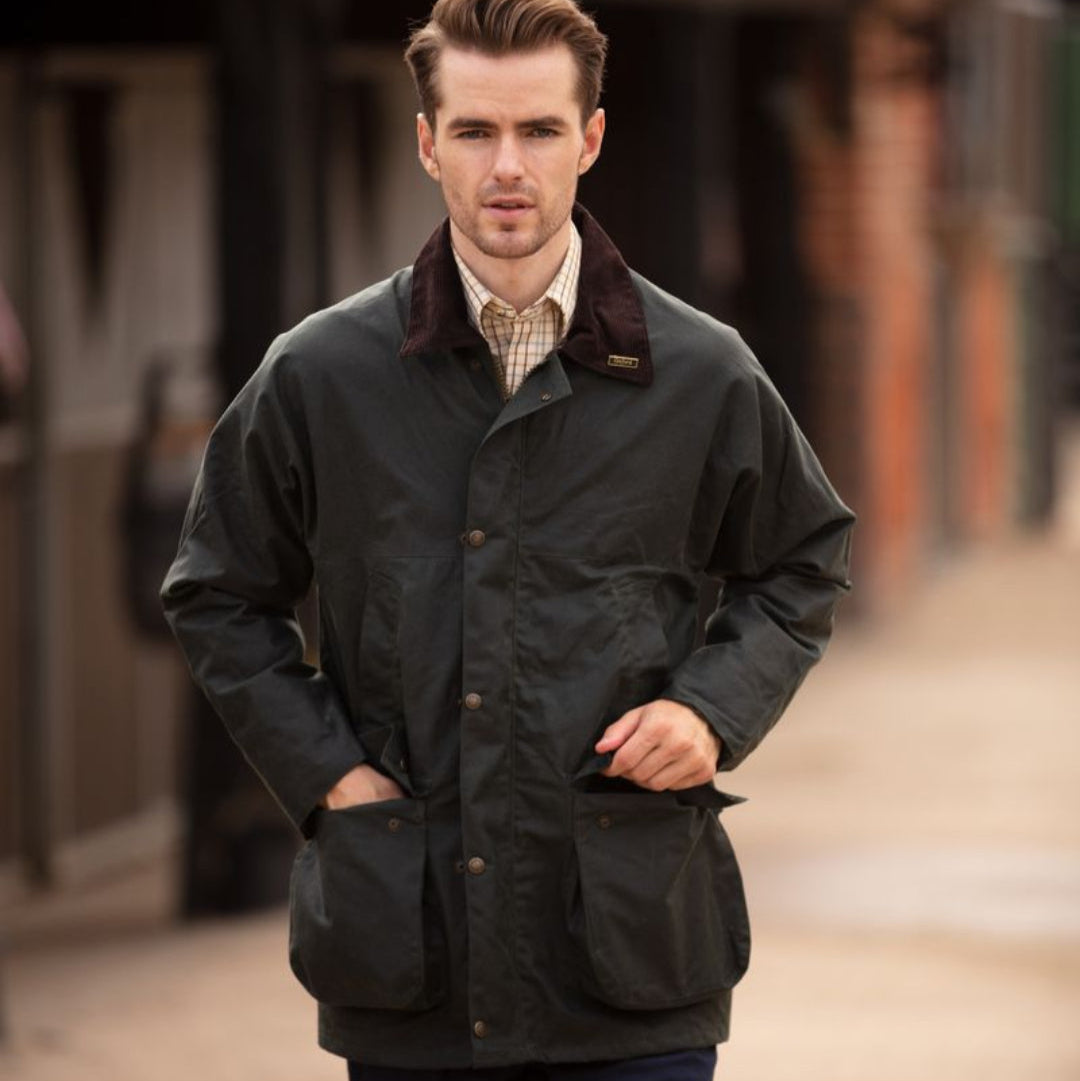 A man wearing a green waxed cotton jacket with a corduroy collar, 2-way zipper, and patch pockets.