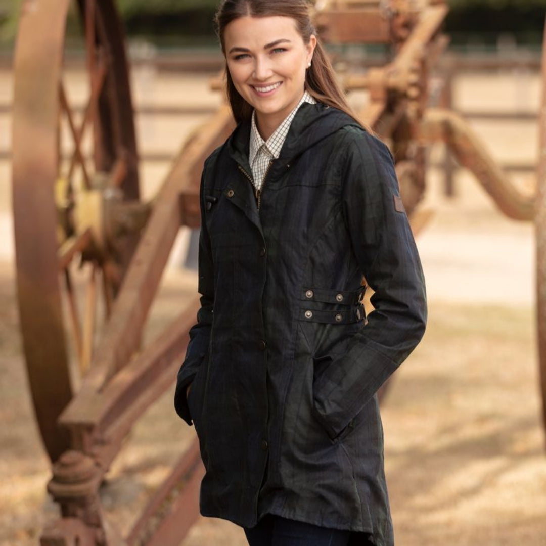 A woman smiling and wearing a wax cotton hooded jacket with adjustable side straps and Black Watch design